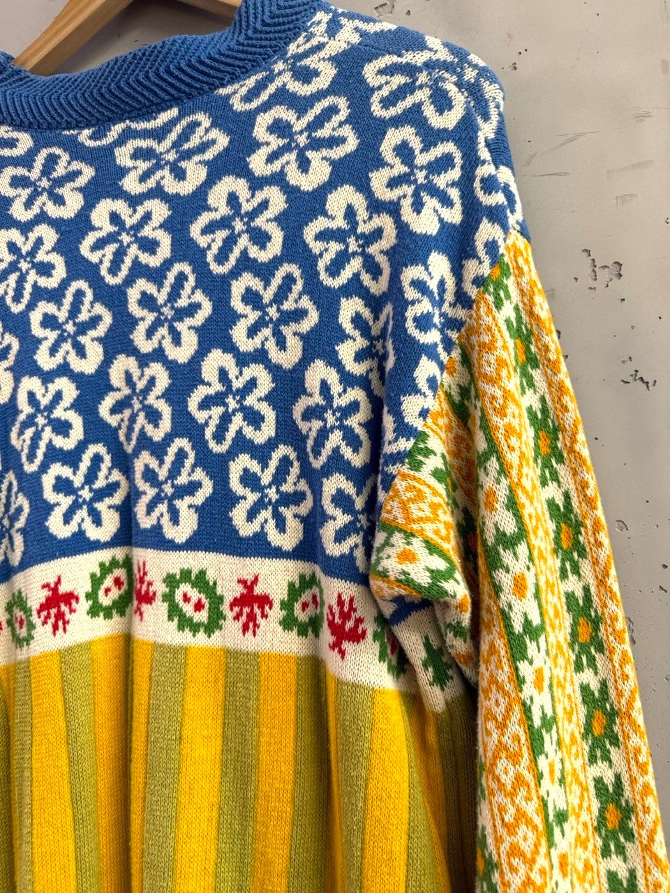BERLIN VINTAGE CORNER blue knit sweater with white floral pattern, red and green accents, and yellow/green stripes. Geometric sleeves.