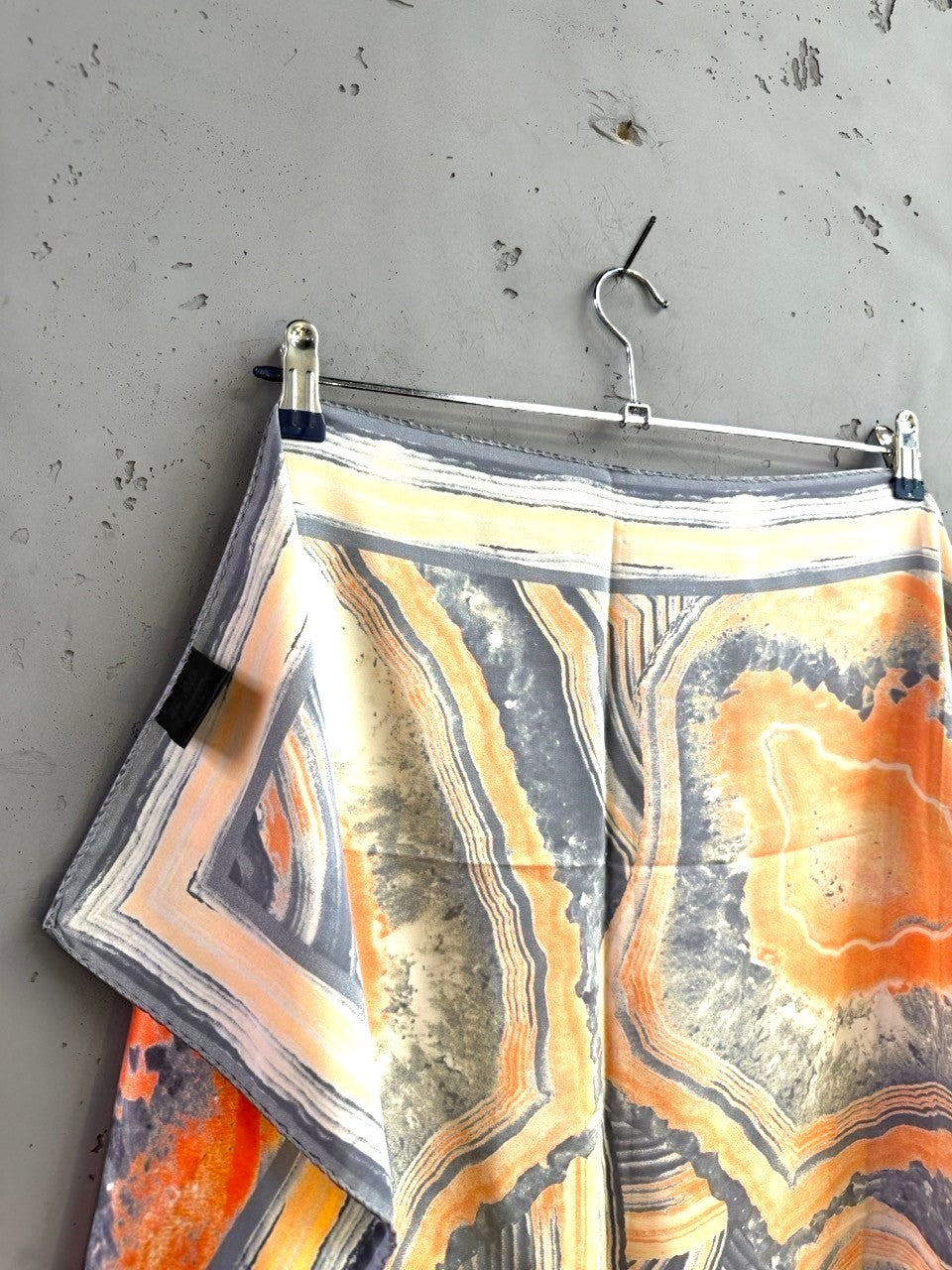 BERLIN VINTAGE CORNER silk scarf with abstract geode print in burnt orange, charcoal, and cream on a grey wall.