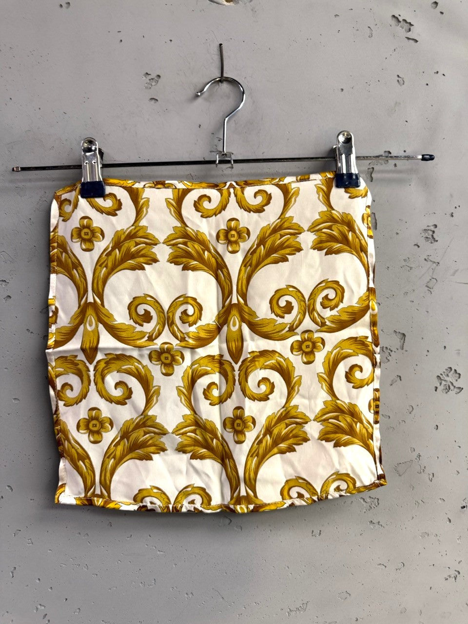 BERLIN VINTAGE CORNER silk pocket square with gold and cream baroque acanthus leaf print on a grey wall background.