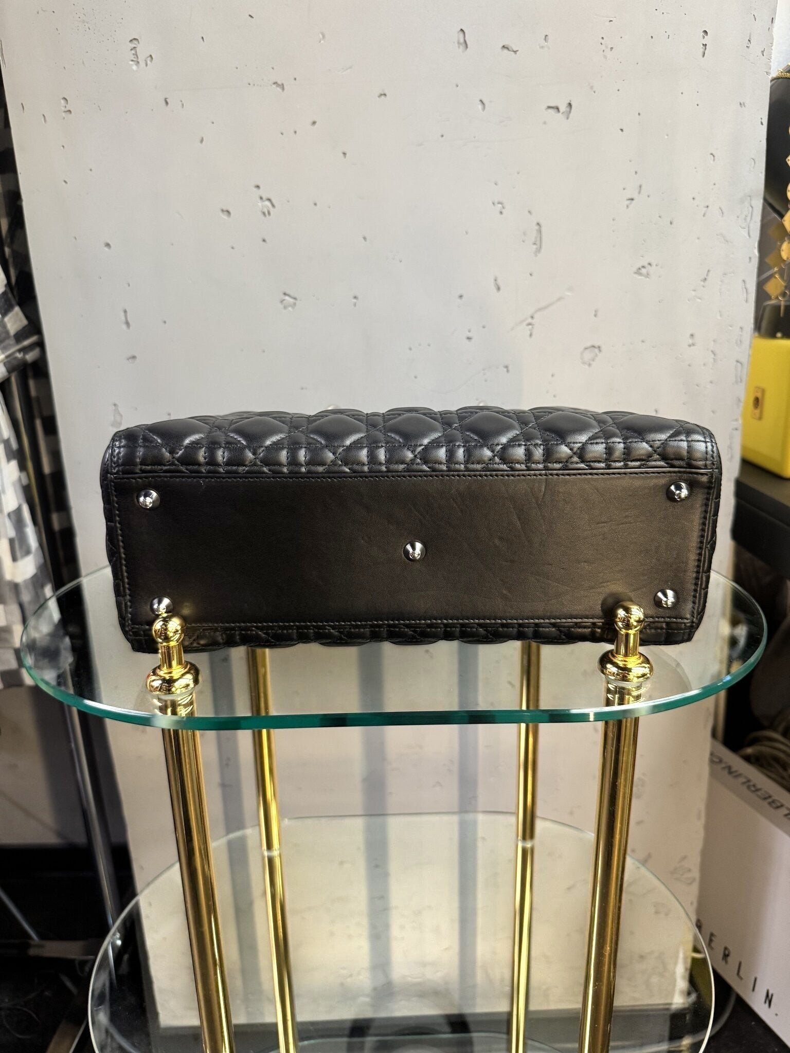BERLIN VINTAGE CORNER black quilted leather handbag base with silver hardware feet on a glass display table