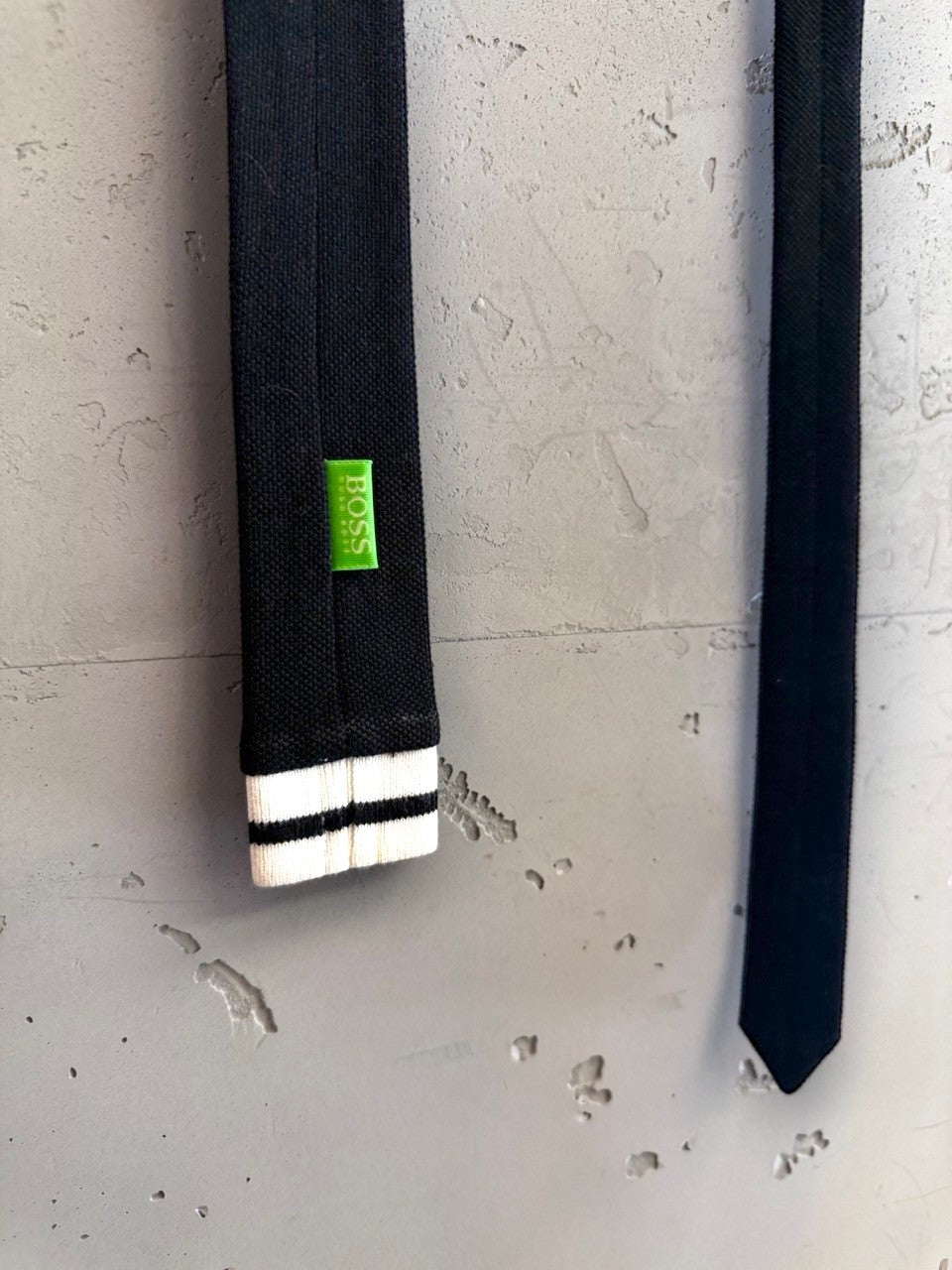 BERLIN VINTAGE CORNER black necktie with white stripes at the tip and a green BOSS logo tag.