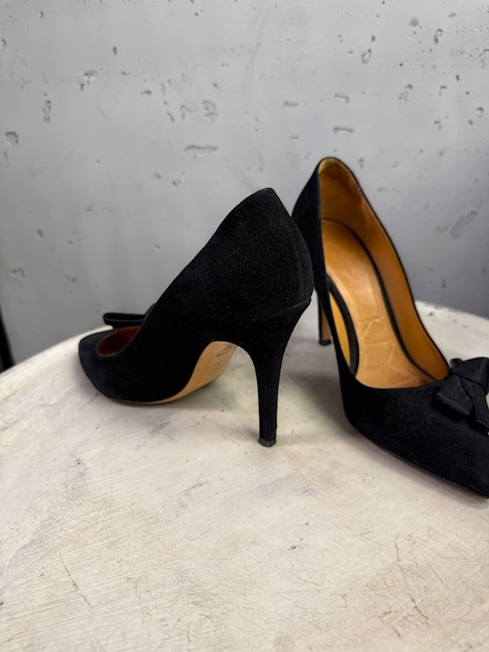 BERLIN VINTAGE CORNER black suede stiletto pumps with pointed toes and bow accents on a white textured surface