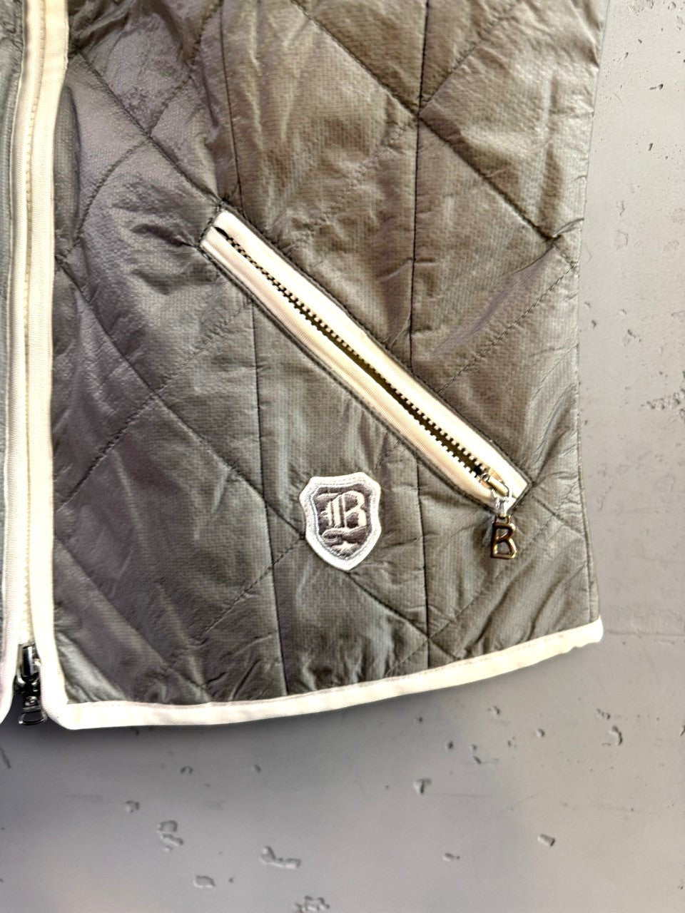 BERLIN VINTAGE CORNER Bogner grey diamond-quilted vest with white piping, zippered pocket, and brand emblem.