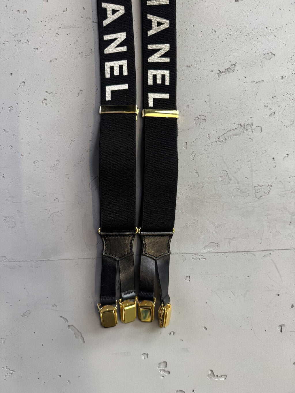 BERLIN VINTAGE CORNER black elastic CHANEL suspenders with white logo text, gold-tone hardware, and leather detailing.
