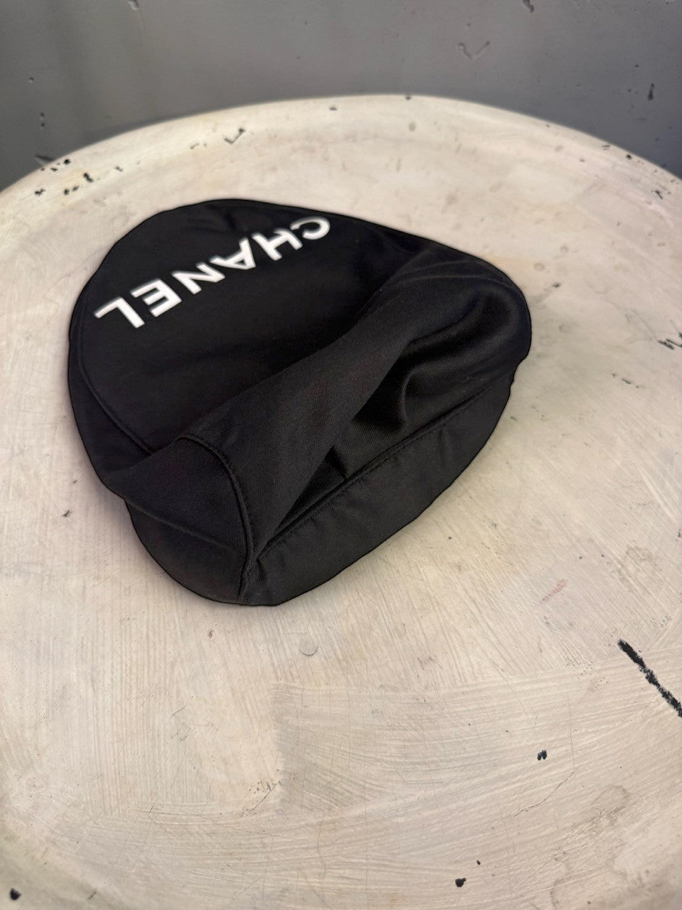 BERLIN VINTAGE CORNER black CHANEL newsboy cap with white logo lettering on a textured white surface