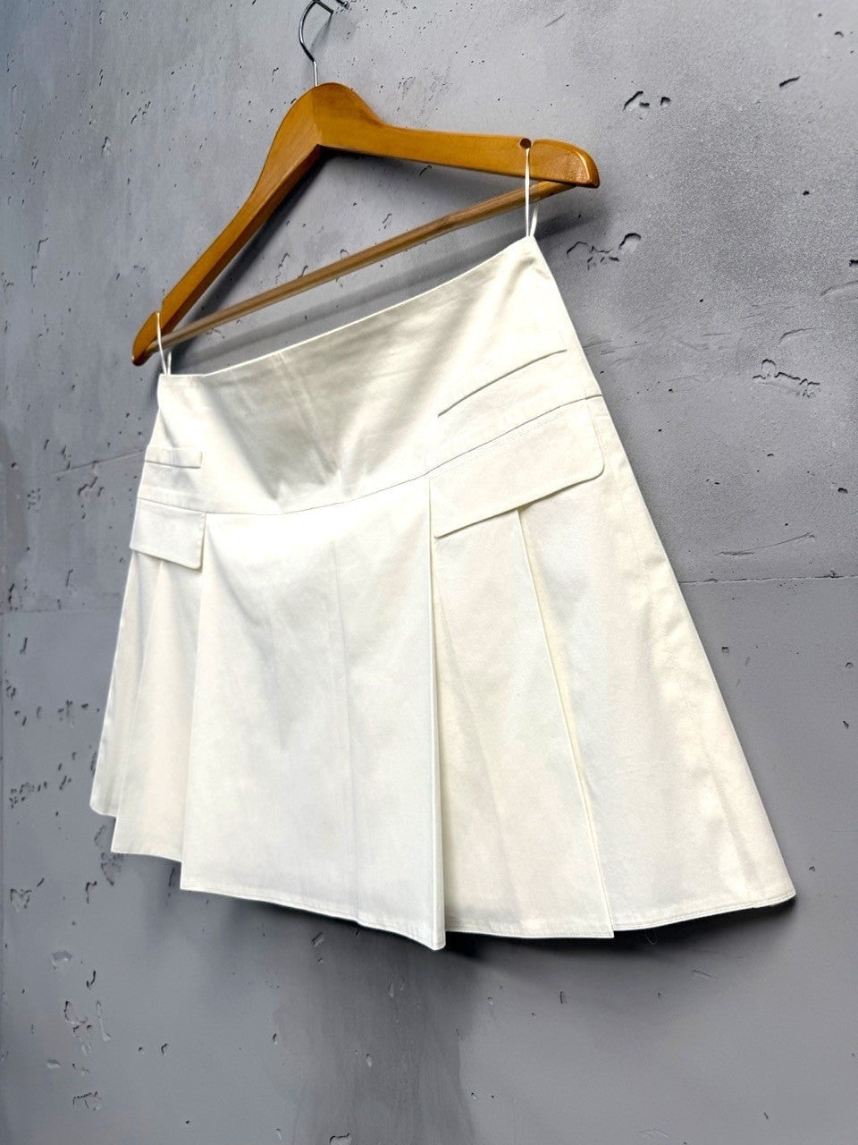 BERLIN VINTAGE CORNER cream high-waisted pleated mini skirt with concealed back zipper and decorative pocket details.