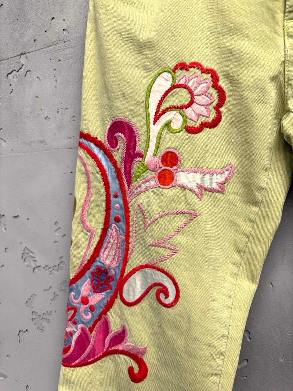 BERLIN VINTAGE CORNER light yellow denim flare jeans with embroidered paisley design in pink, red, and blue on the left leg.