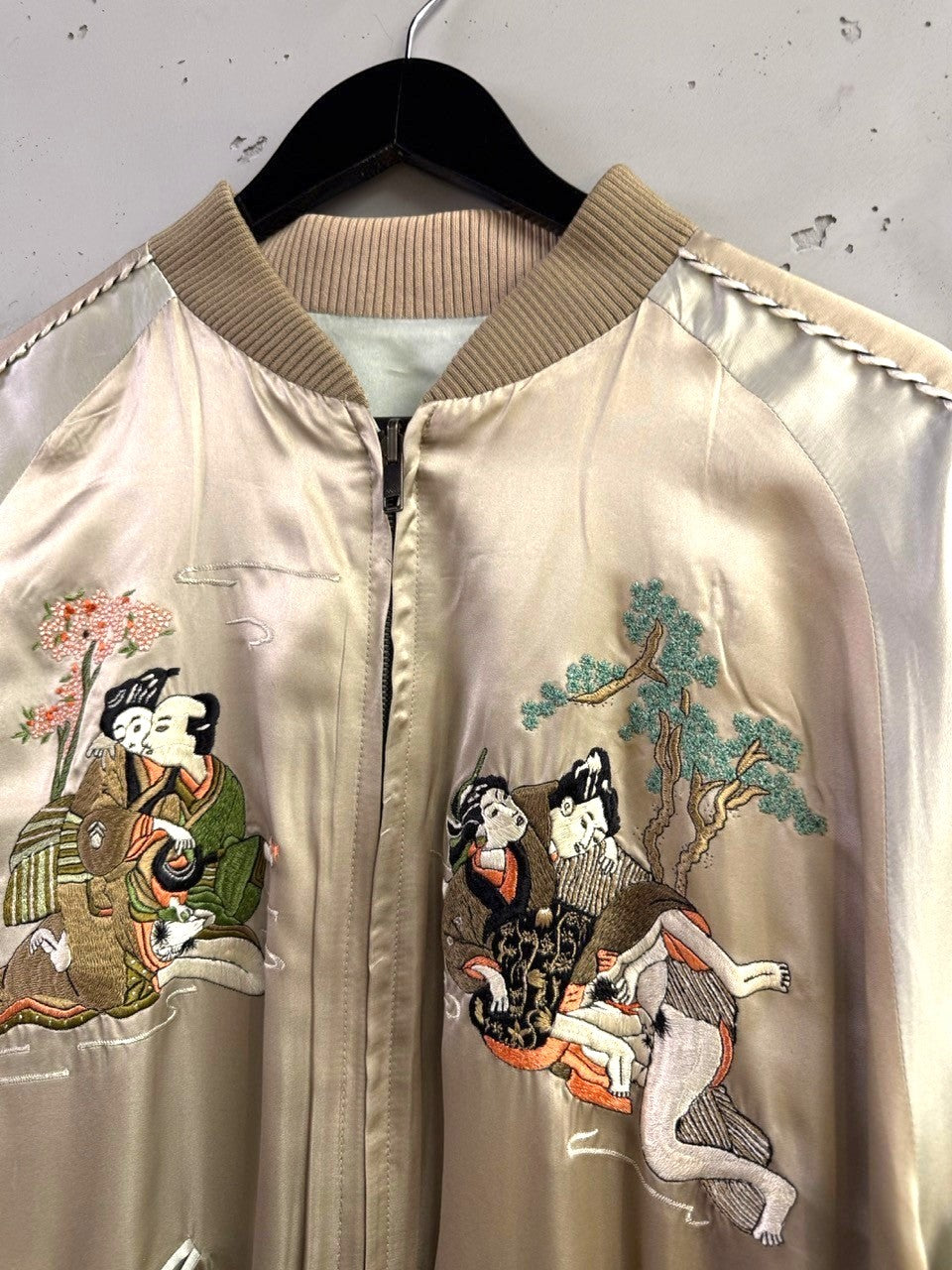 BERLIN VINTAGE CORNER champagne satin bomber jacket with traditional Japanese embroidery of figures and cherry blossoms. Ribbed collar, cuffs, and hem.