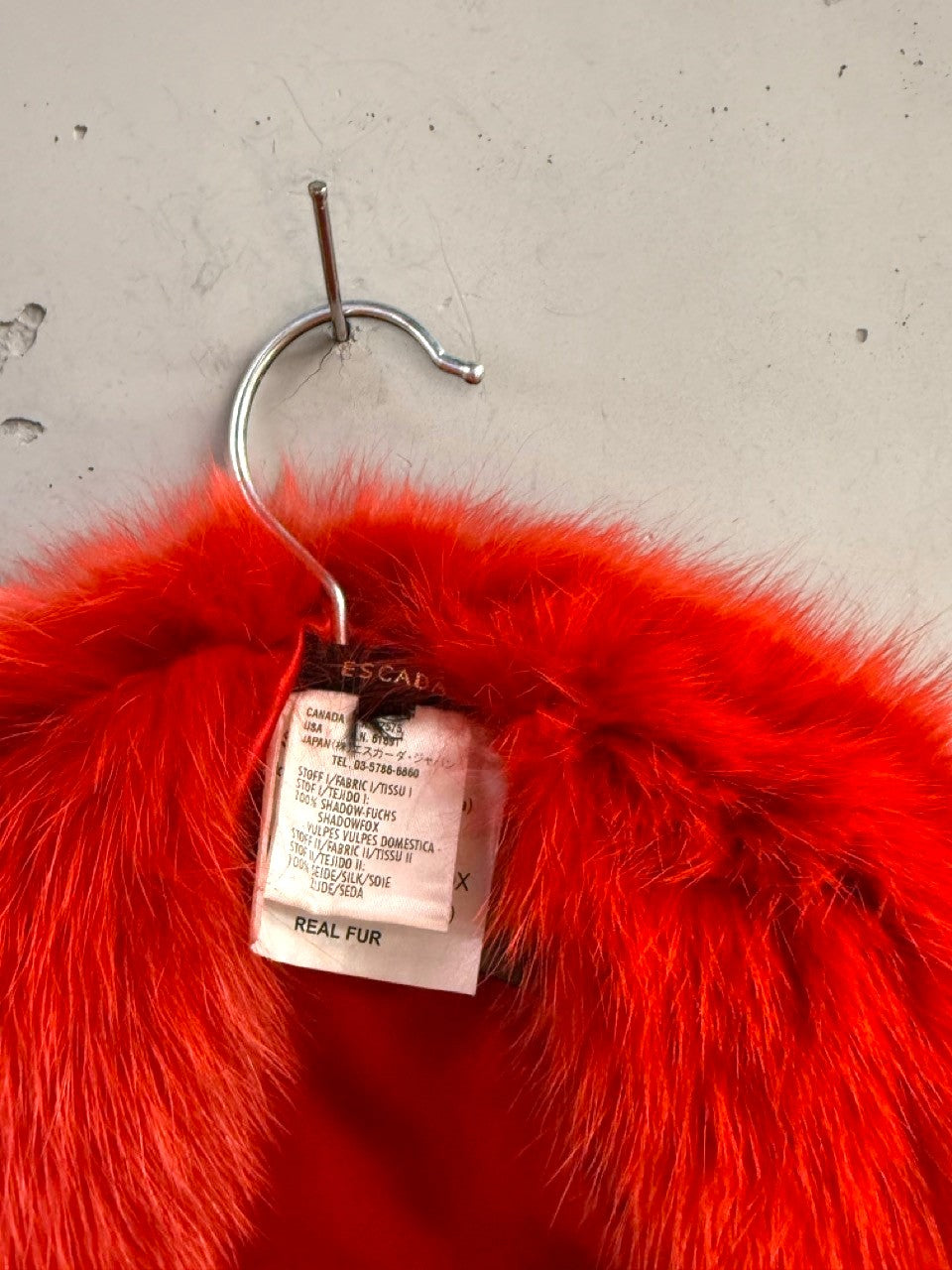 BERLIN VINTAGE CORNER Escada red shadow fox fur collar with silk lining and brand tag hanging on a hook.