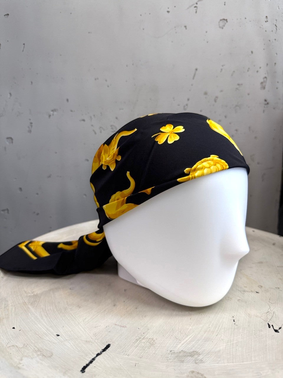 BERLIN VINTAGE CORNER Escada silk scarf in black with golden elephant, turtle, and clover print on a mannequin head.