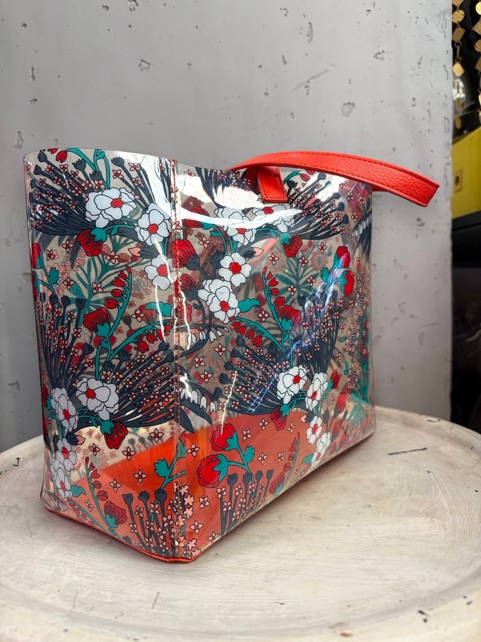 BERLIN VINTAGE CORNER transparent PVC tote bag with red, teal, and white floral print and orange textured handles.