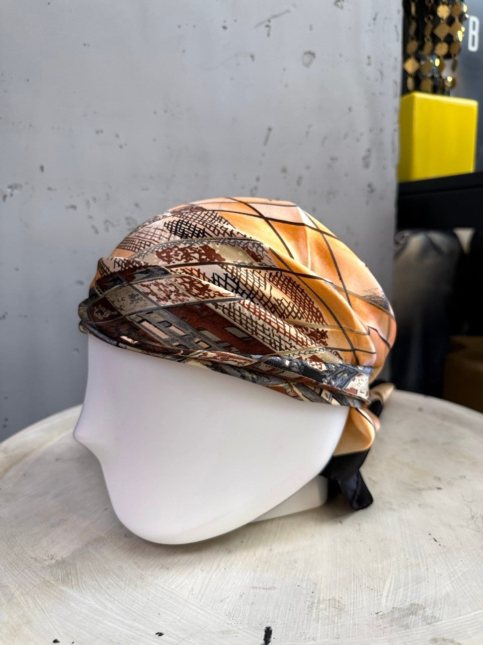 BERLIN VINTAGE CORNER silk scarf with a geometric pattern in peach, black, and earth tones styled as a headwrap.
