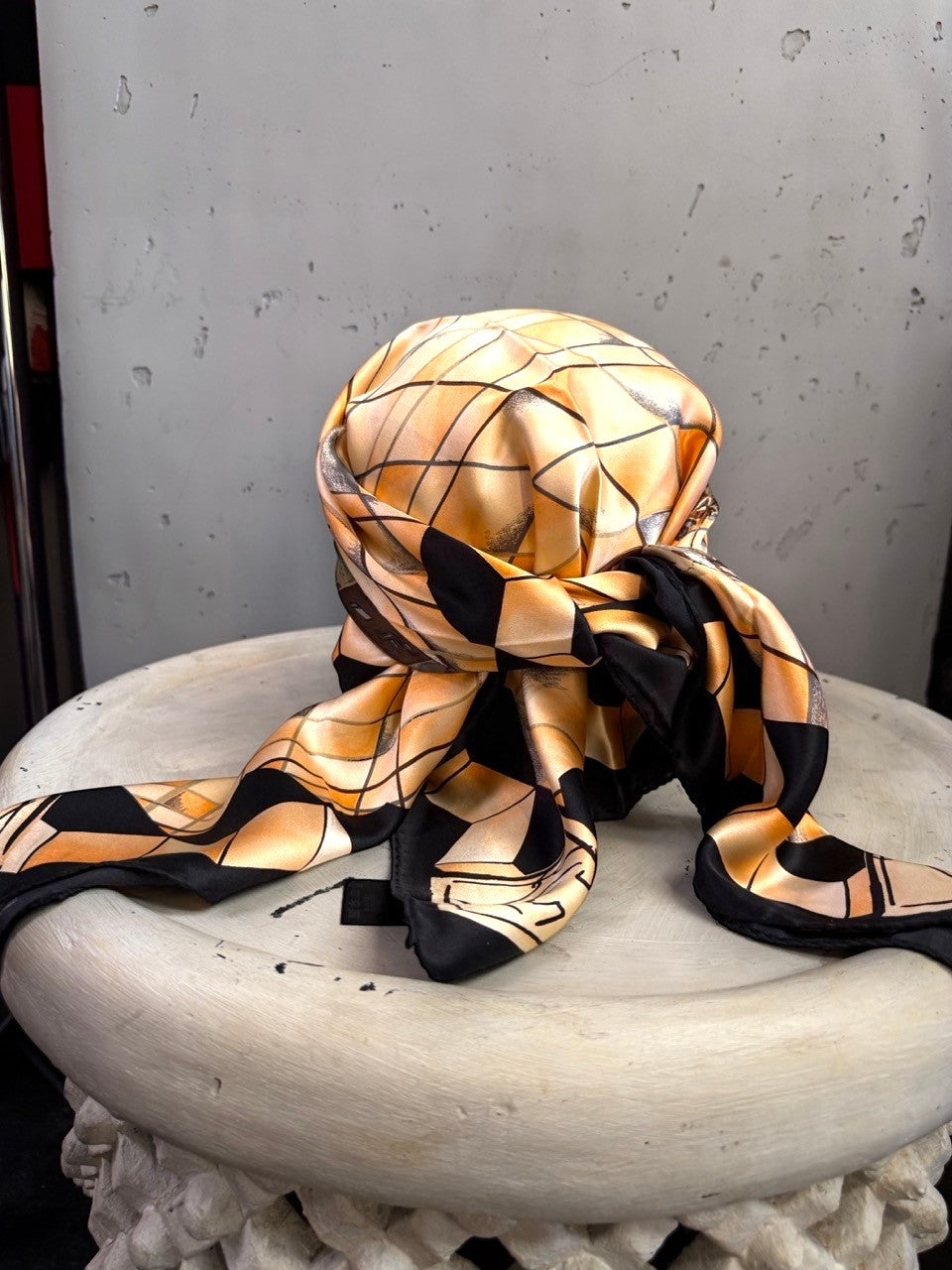 BERLIN VINTAGE CORNER silk scarf with a geometric peach and black pattern, styled as a headscarf on a white pedestal.