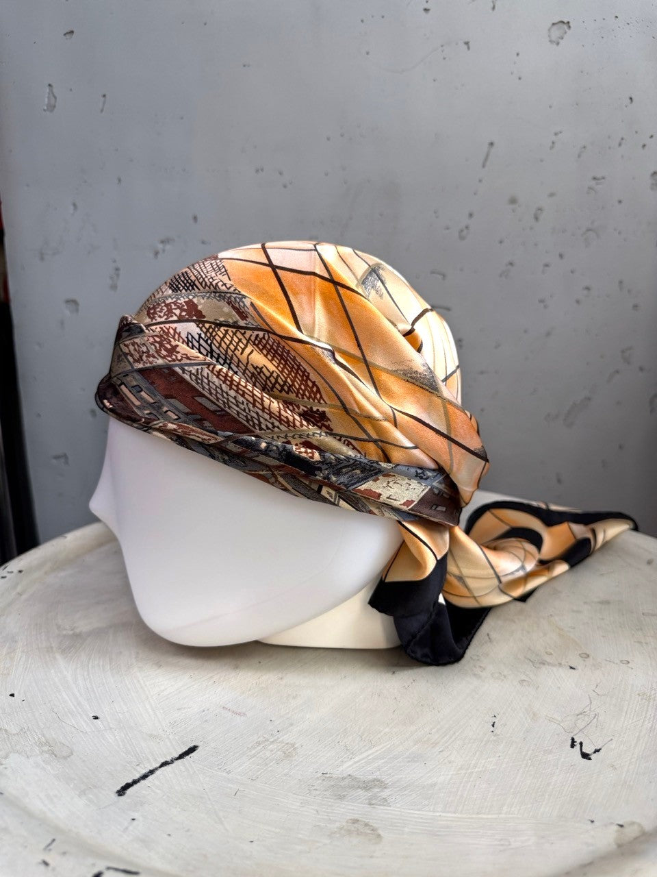 BERLIN VINTAGE CORNER silk scarf with geometric pattern in peach, black, and earth tones styled as a headwrap