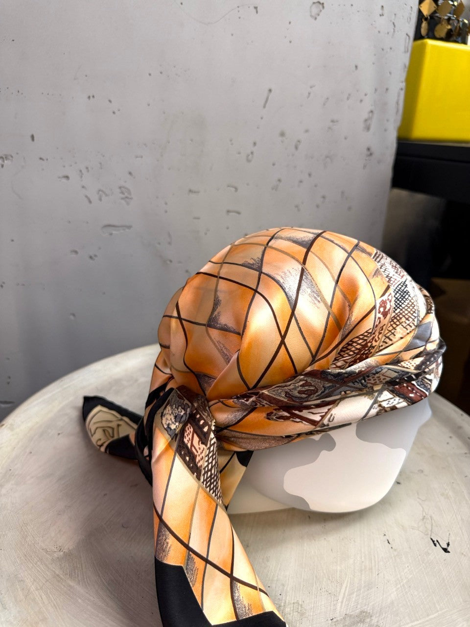 BERLIN VINTAGE CORNER silk scarf with a peach and black geometric grid pattern draped on a mannequin head.