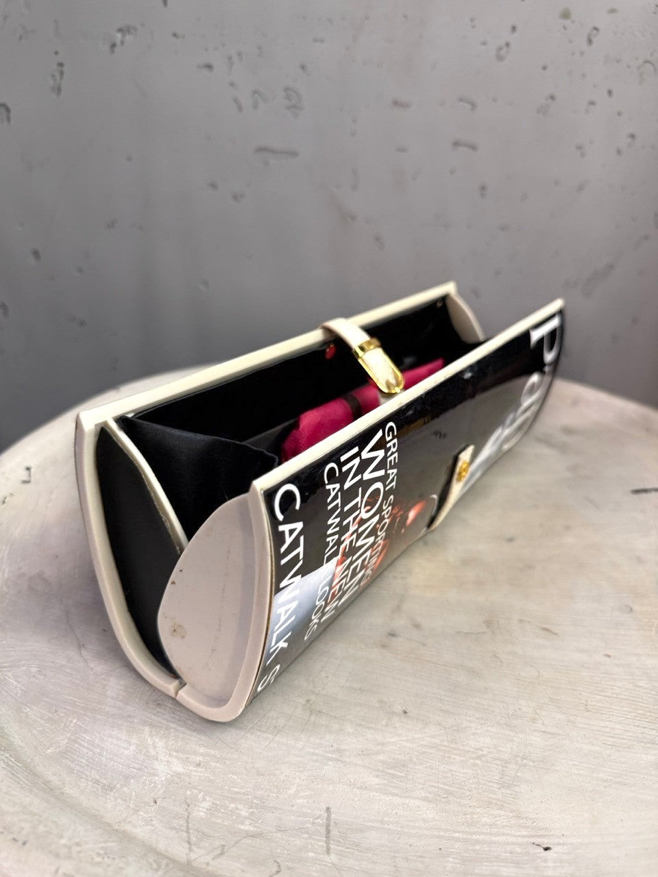 BERLIN VINTAGE CORNER hard shell clutch with magazine graphic print, cream frame, and gold buckle strap.