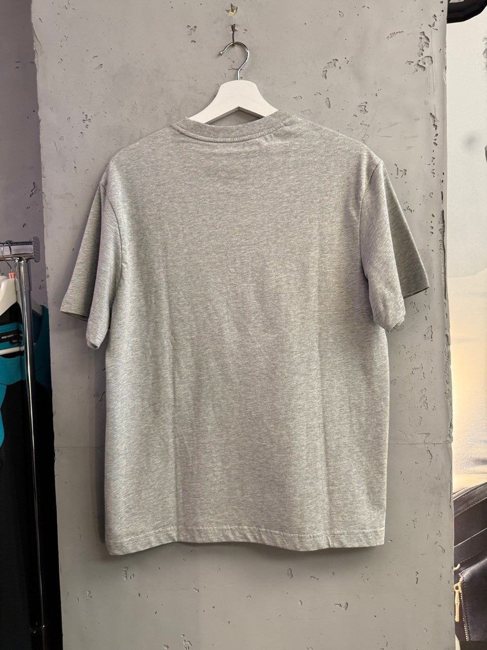 BERLIN VINTAGE CORNER heather grey cotton crewneck t-shirt, back view hanging on a white hanger against a concrete wall.