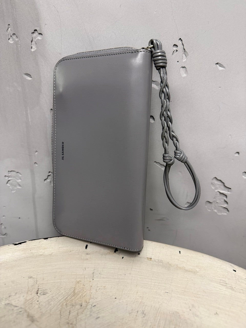 BERLIN VINTAGE CORNER grey leather zip-around wallet with braided wristlet strap and embossed logo.
