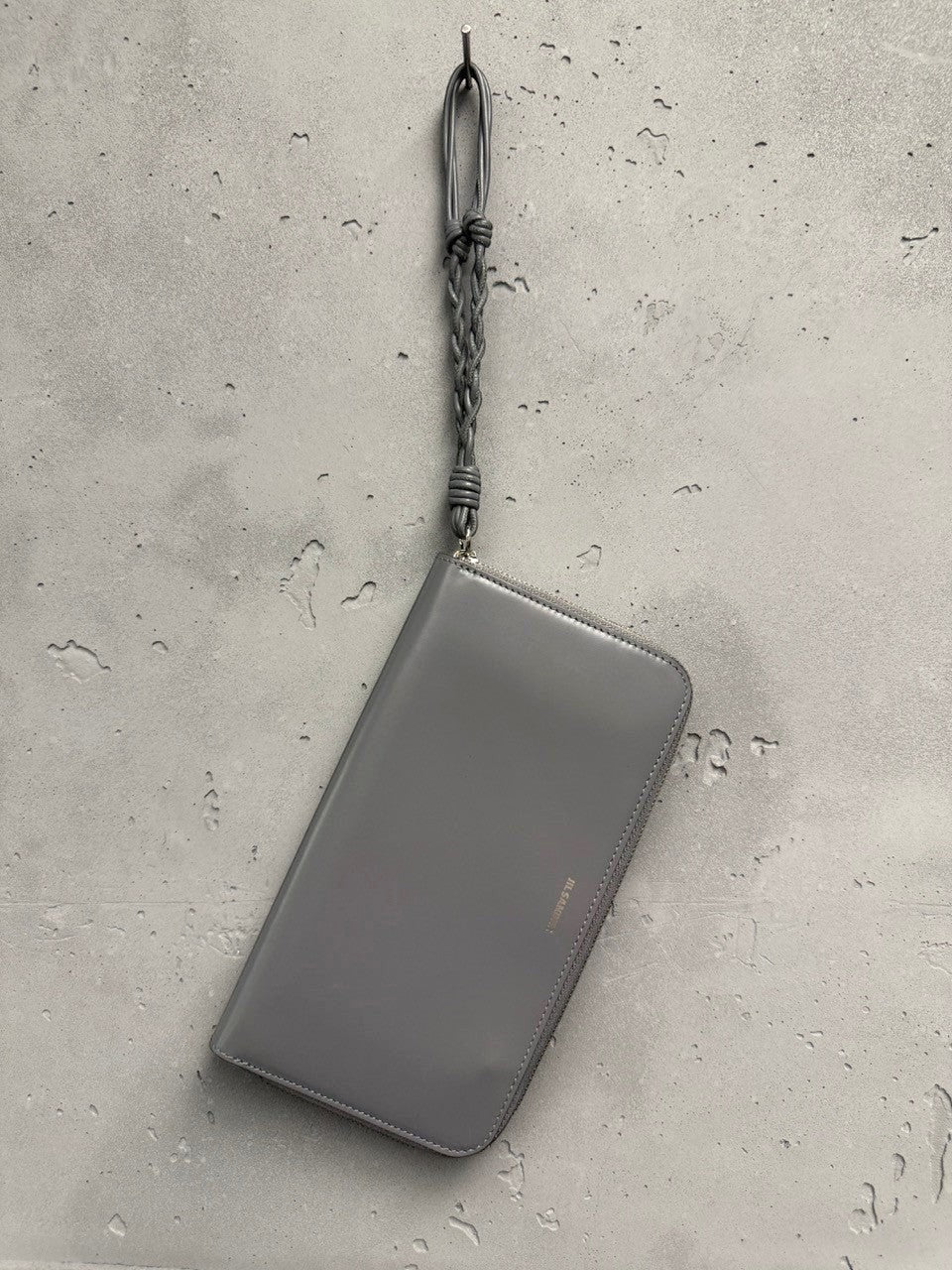 BERLIN VINTAGE CORNER grey polished leather zip-around wallet with braided wristlet strap and embossed logo.