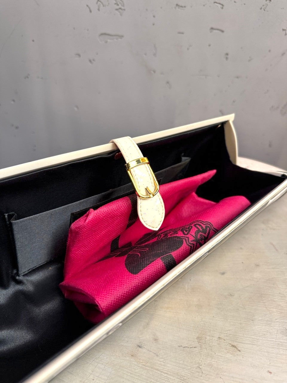 BERLIN VINTAGE CORNER hard shell clutch with cream strap, gold buckle, and black interior lining.