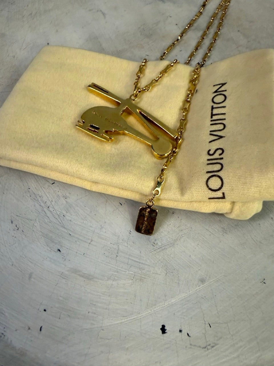 BERLIN VINTAGE CORNER gold-tone helicopter pendant necklace with small embossed charm and Louis Vuitton pouch.