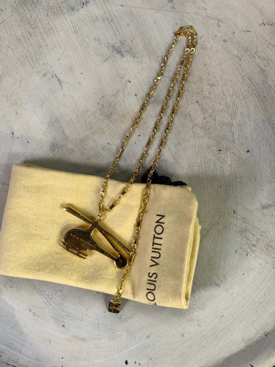 BERLIN VINTAGE CORNER gold-tone helicopter pendant necklace with a small embossed charm and Louis Vuitton pouch.