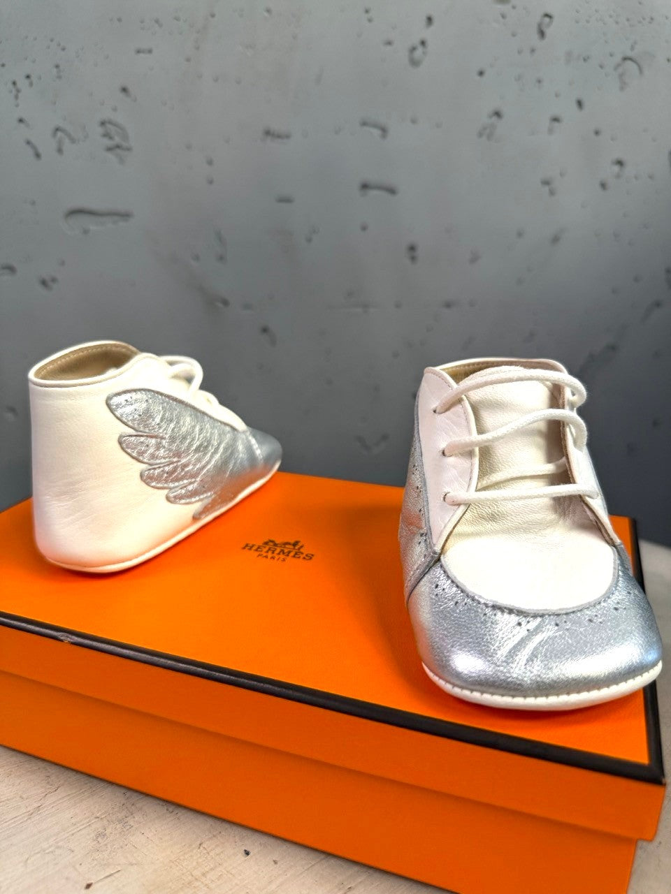BERLIN VINTAGE CORNER Hermès infant lambskin lace-up booties in white and metallic silver with wing side detail.