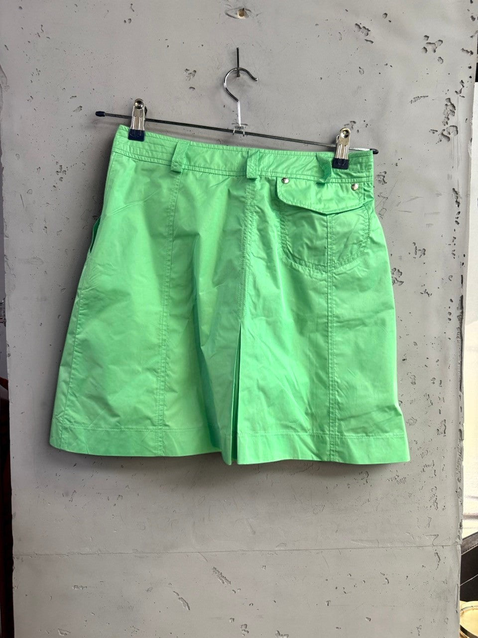 BERLIN VINTAGE CORNER lime green pleated mini skirt with belt loops and back pocket, hanging on a hanger.
