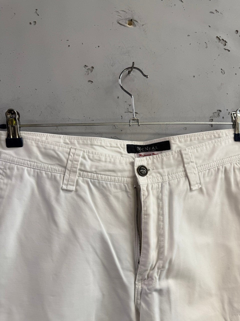 BERLIN VINTAGE CORNER McNEAL white cotton cargo shorts with button closure and zip fly hanging on a metal hanger.