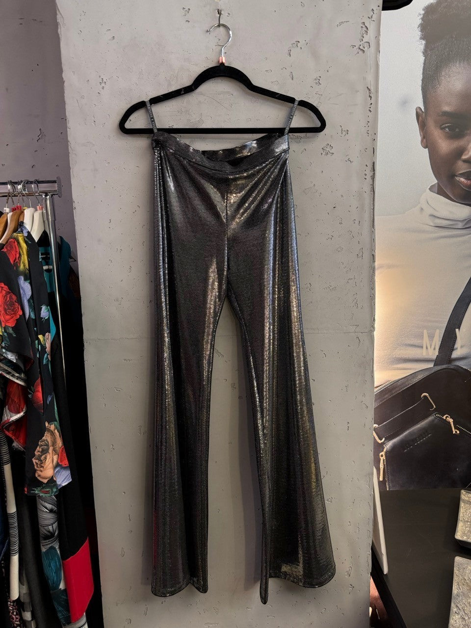 BERLIN VINTAGE CORNER metallic silver wide-leg trousers hanging on a black hanger against a textured wall.