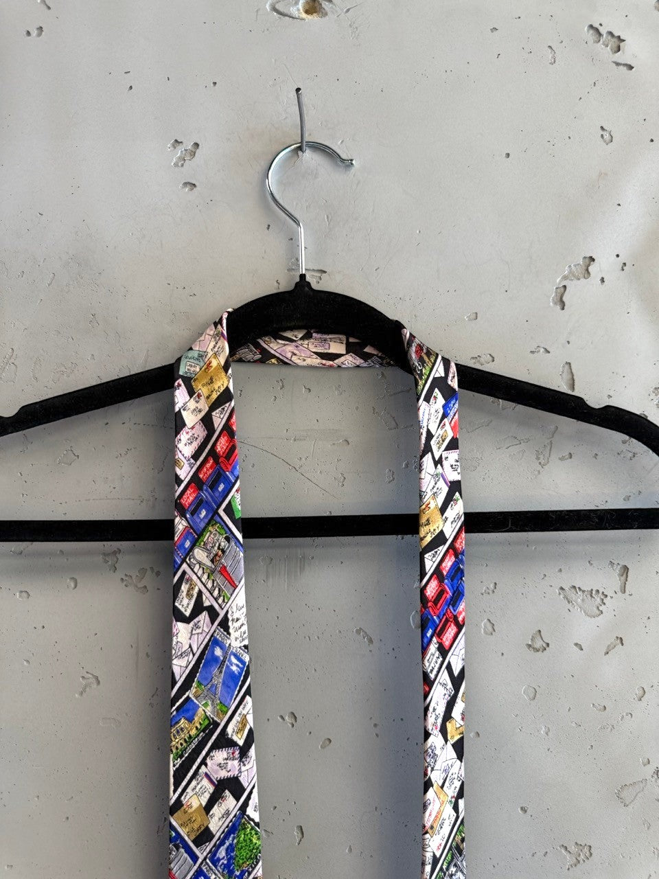 Nicole Miller 1992 silk necktie with a black background featuring a collage of envelopes, stamps, and landmarks like the Eiffel Tower.