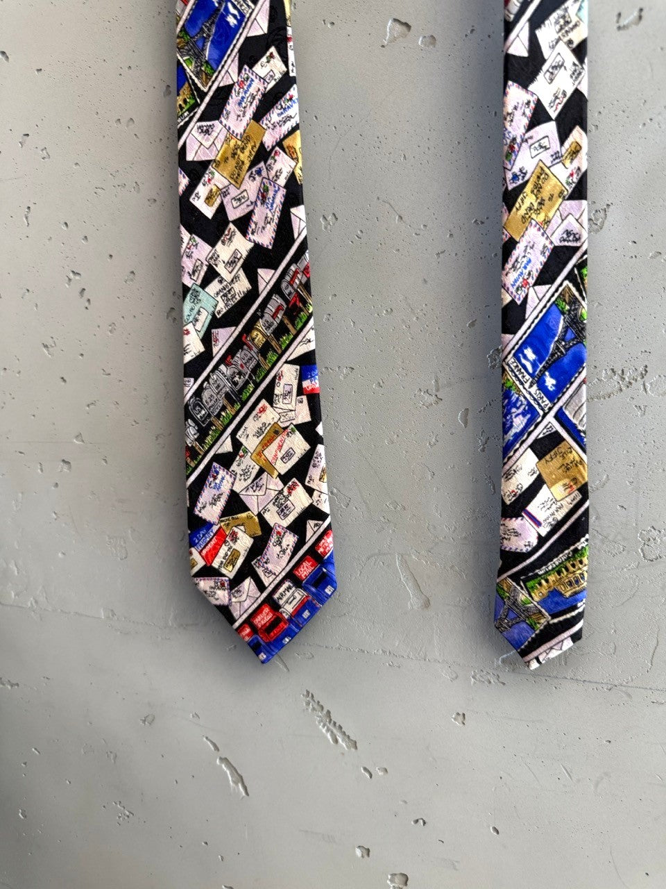 BERLIN VINTAGE CORNER Nicole Miller 1992 silk necktie with a black background and a collage print of envelopes, stamps, and landmarks.