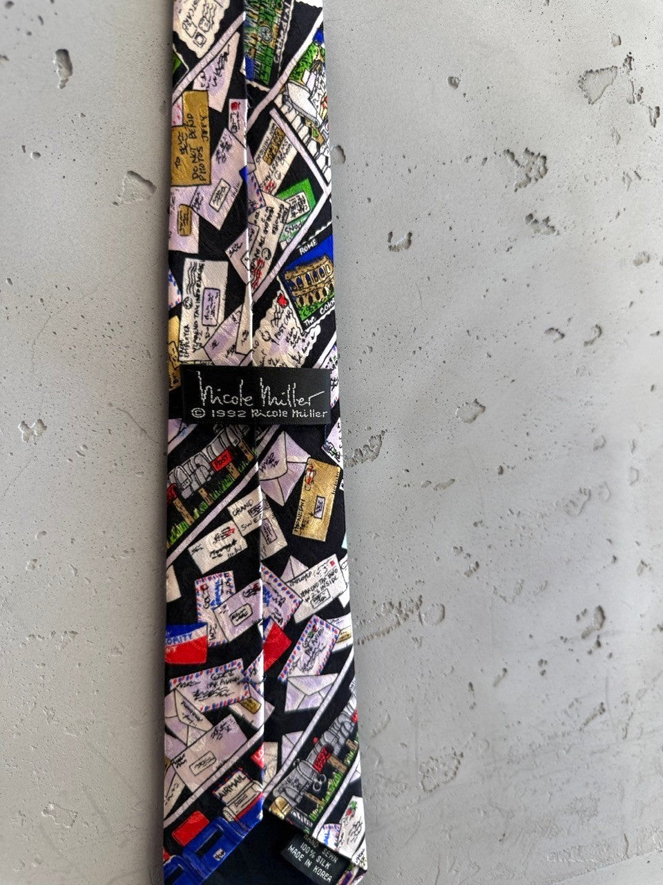 BERLIN VINTAGE CORNER Nicole Miller 1992 silk necktie with black background and 'Letters from Around the World' print.