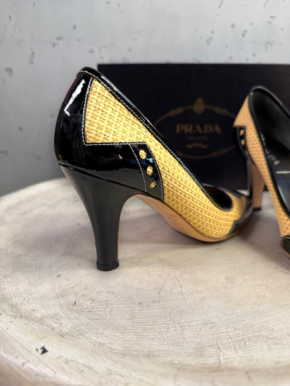 BERLIN VINTAGE CORNER Prada pumps in woven raffia and black patent leather with stud details on a white textured base.