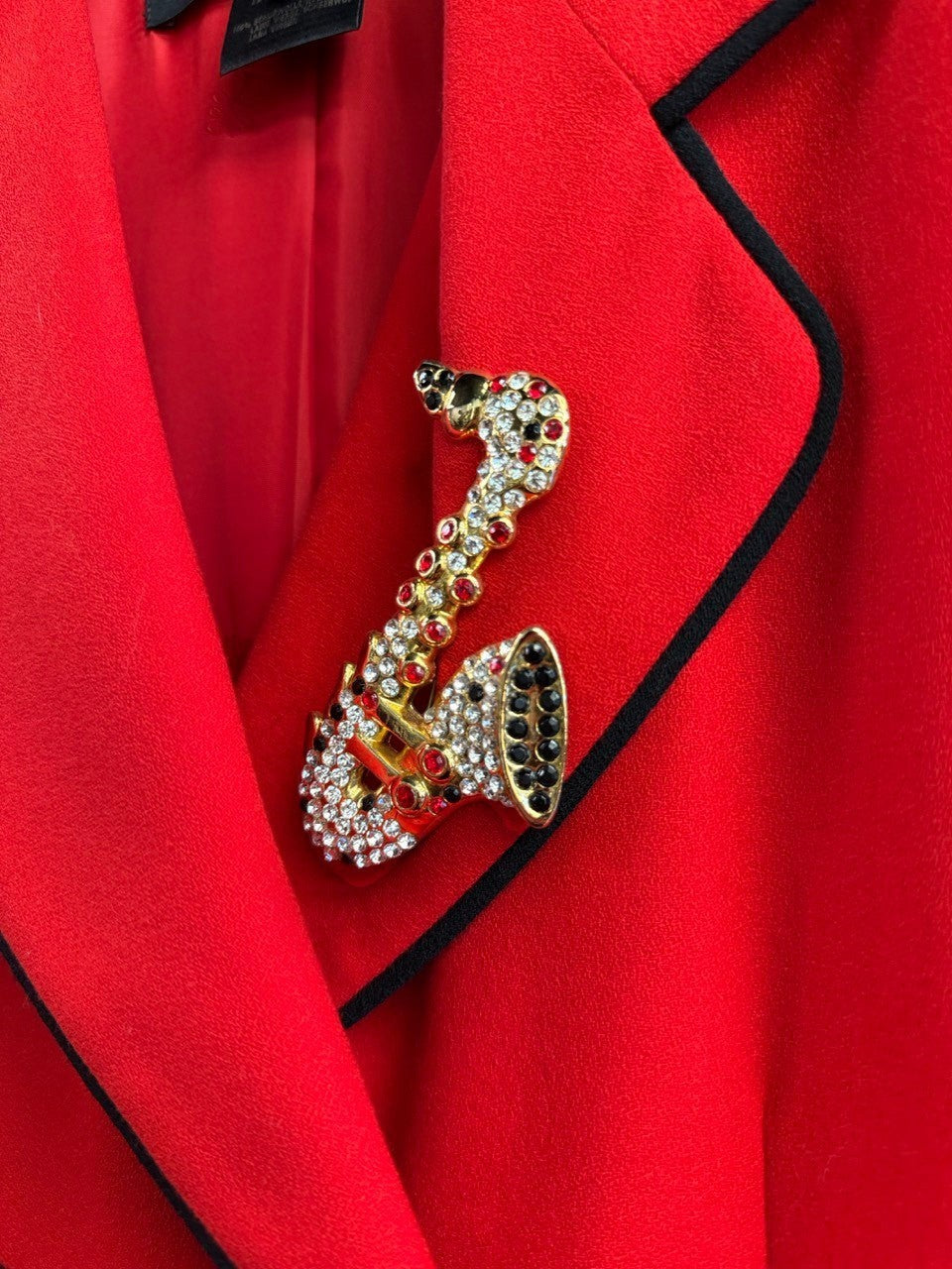 BERLIN VINTAGE CORNER red wool blend double-breasted blazer with black piping and a rhinestone saxophone brooch.