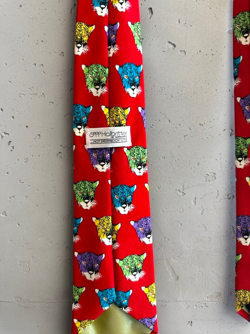 BERLIN VINTAGE CORNER red silk tie with a repeating pattern of colorful jaguar heads in purple, yellow, green, and blue.