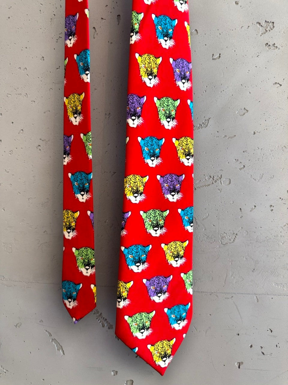 BERLIN VINTAGE CORNER red silk tie with a repeating pattern of colorful jaguar heads in purple, yellow, green, and blue.