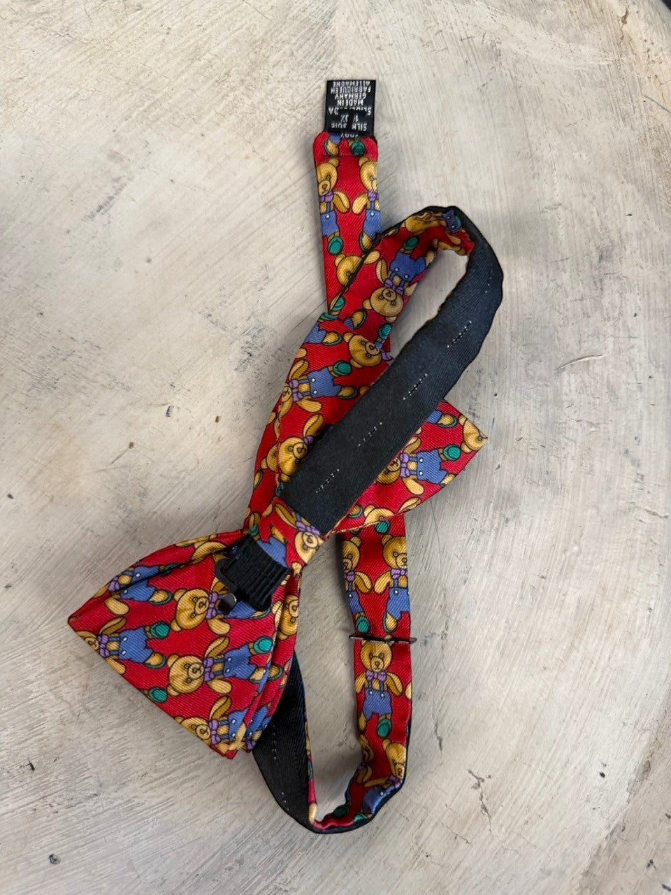 BERLIN VINTAGE CORNER red silk bow tie with a pattern of teddy bears in blue overalls and purple bows. Adjustable strap.