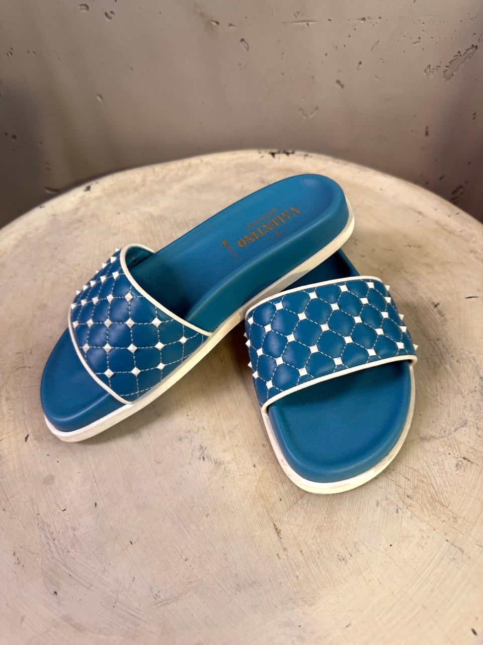 BERLIN VINTAGE CORNER teal slide sandals with white trim and quilted straps adorned with studs.