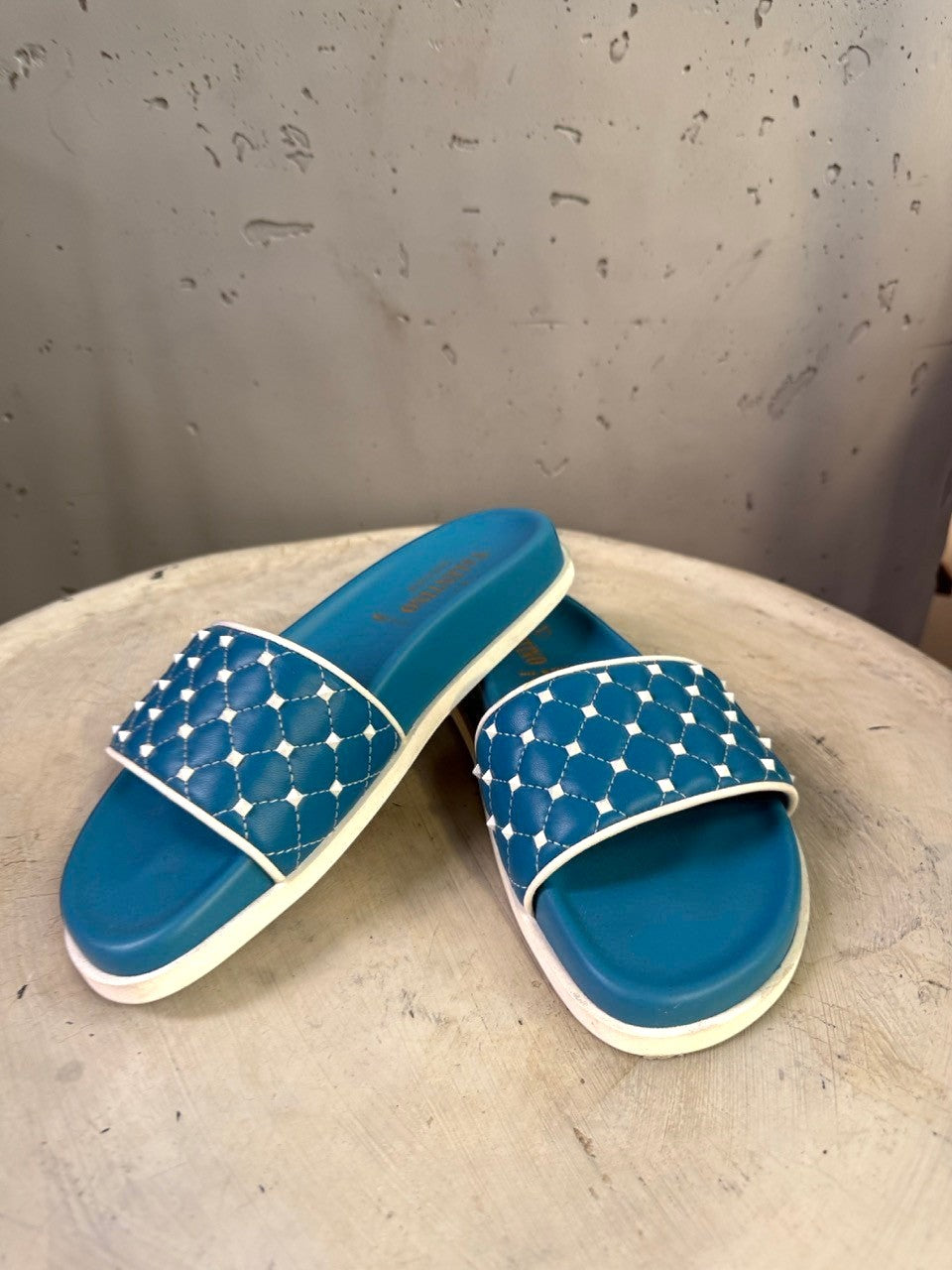 BERLIN VINTAGE CORNER teal slide sandals with white trim and quilted straps adorned with studs.
