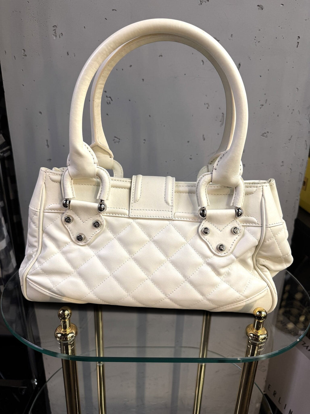 BERLIN VINTAGE CORNER white quilted leather handbag with silver hardware and top handles on a glass display stand.