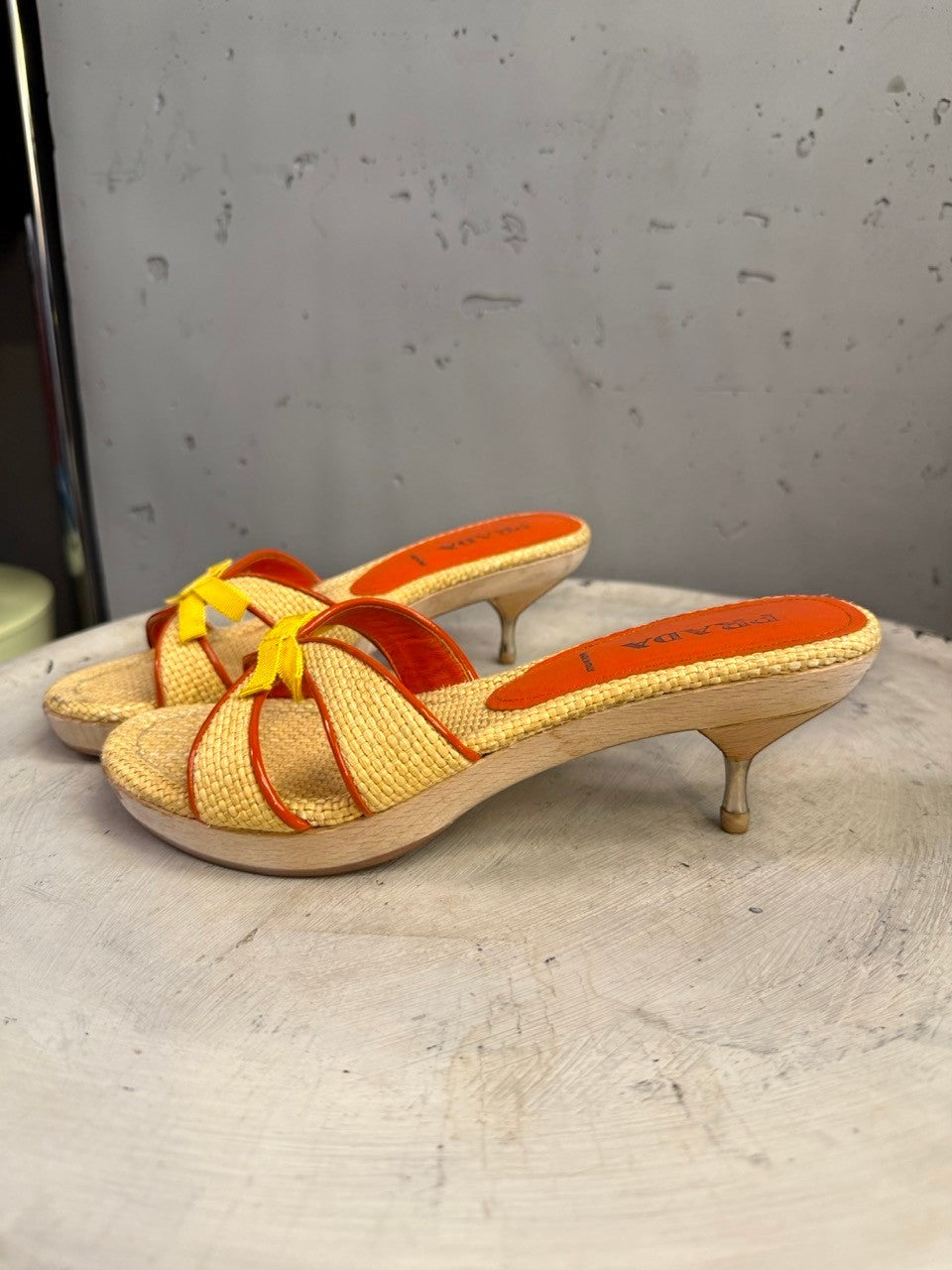 BERLIN VINTAGE CORNER woven raffia slide heeled sandals with orange trim, yellow bow accent, and wooden platform with metallic stiletto heel.